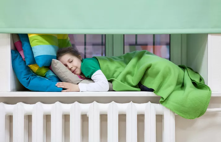 Child asleep on window sill over a radiator