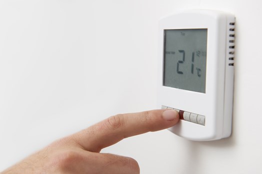 Hand adjusting a digital wall thermostat to 21°C for energy-efficient home heating
