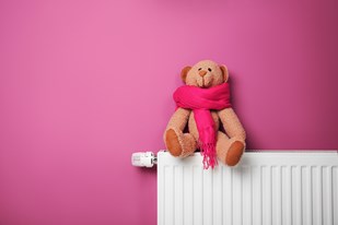 Brown teddy bear in a pink scarf on a radiator symbolizing home heating comfort