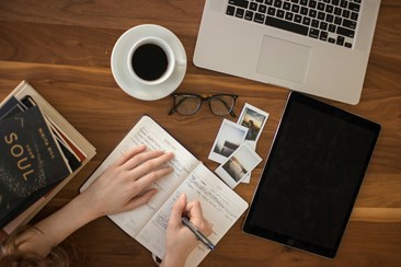 Overhead view of a person writing in a notebook at a desk for organized planning
