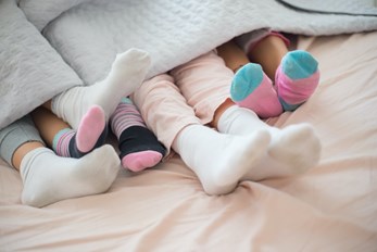 Close-up of feet in colorful socks under a duvet showing the comfort of a warm home